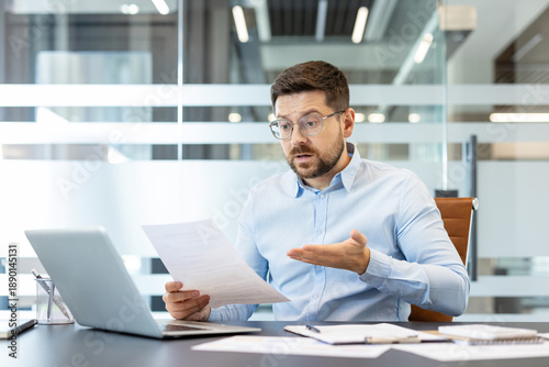 Картината върху платно Confused businessman at office desk reading stressful financial reports and pape