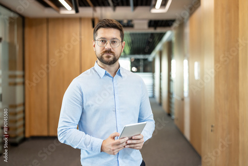 Fotografie Young businessman wearing a blue shirt and eyeglasses standing confidently in a