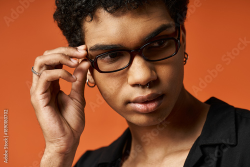 Tablou pe pânză Stylish young Black man confidently adjusting his glasses in a vibrant studio