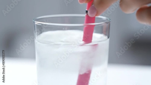 Pink stirrer in a clear glass with cloudy liquid and a hand