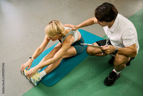 Fotografie Middle aged Caucasian woman performing seated hamstring stretch on exercise mat,