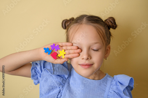 Child holding colorful puzzle pieces near face. Autism awareness concept, inclusion, diversity, equality and social support on yellow background.