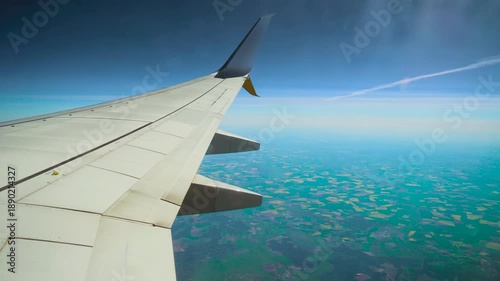 Passenger airplane flying under chemtrail over patchwork fields. Jet cruising beneath white trail across farmland mosaic. Aircraft gliding below vapor line above agricultural landscape