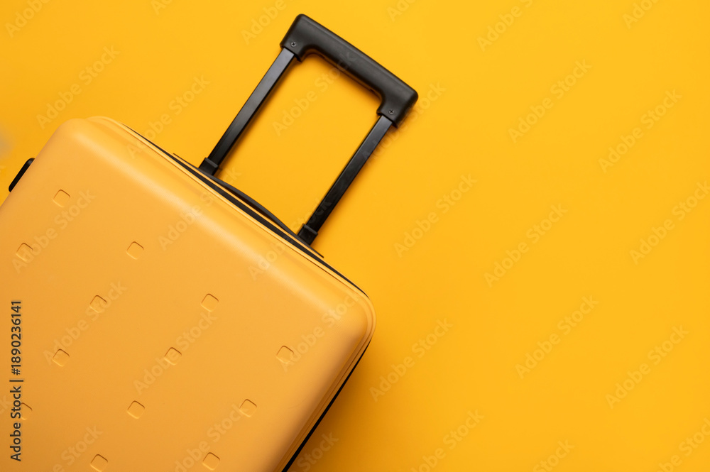 Fototapeta premium Travel, vacation, trip, and flight concept. Stylish yellow plastic suitcase with black handle on yellow background, flat lay top view. Baggage, comfortable suitcase for clothes, minimalist summer back