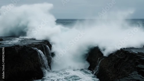 Crashing ocean waves against dark rocks, dramatic sea spray, and turbulent water.
