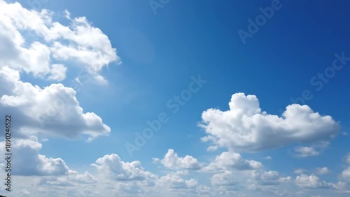 Cumulus clouds drift across a clear blue sky on a sunny day