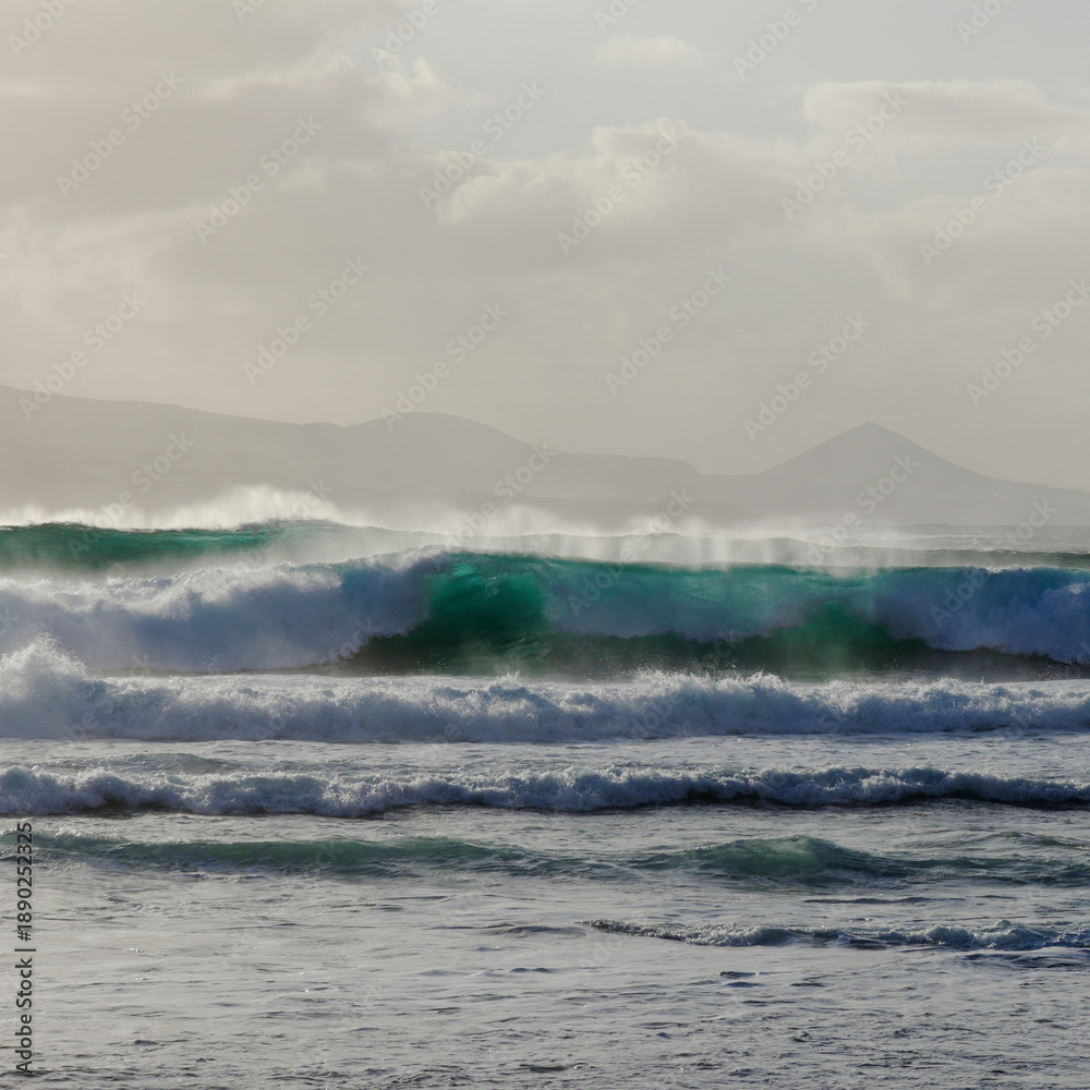 Fototapeta premium Gran Canaria, view towards Atlantic ocean from El Confital beach on the edge of Las Palmas de Gran Canaria, big waves crushing, rain in the mountains 