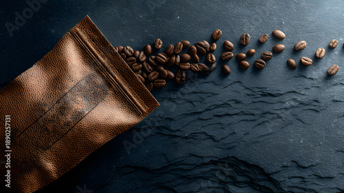 Roasted coffee beans spilling from a textured brown leather pouch onto a dark slate surface with dramatic side lighting