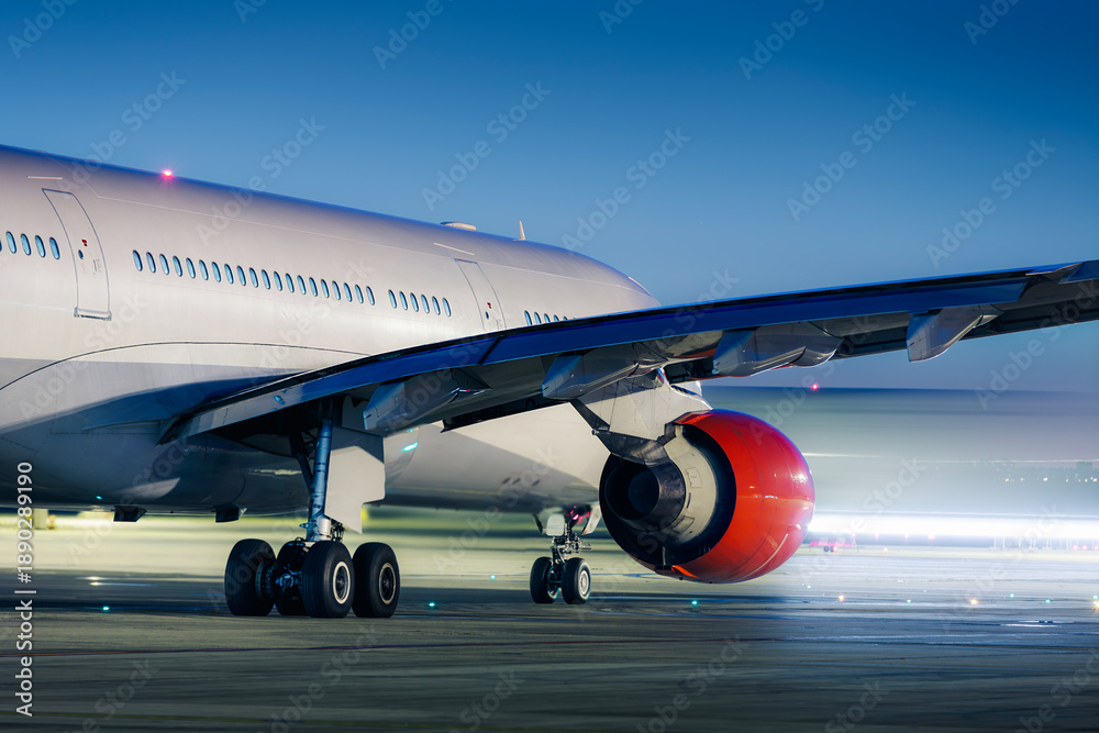 Obraz premium Commercial airplane taxiing on airport runway at night while another aircraft creates motion blur light trail. Air travel, speed, and transportation during night operations.