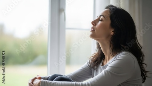 Relaxed woman sitting by window enjoying peaceful moment at home
