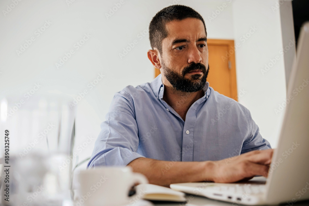 © kleberpicui - Focused adult business man working on a laptop while sitting at a desk in a home office. Concepts of remote work, freelance lifestyle, productivity, technology, modern professional and work from home © kleberpicui - Focused adult business man working on a laptop while sitting at a desk in a home office. Concepts of remote work, freelance lifestyle, productivity, technology, modern professional and work from home