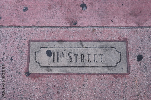 Sign for 11th street set into the red tinted concrete of a sidewalk in the south part of the USA. 