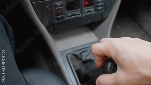 Closeup of a person's hand shifting the manual gear stick of an older car, moving through the different speeds while driving and showing the control and skill required for stick shift operation