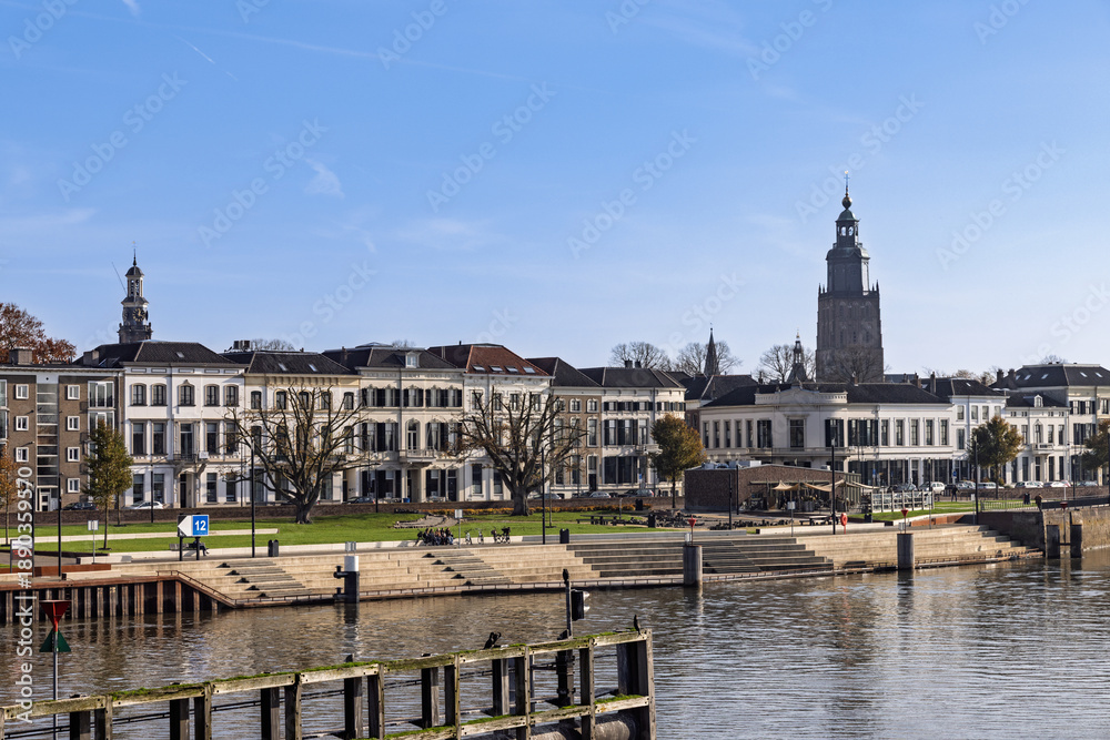 Fototapeta premium Zutphen city skyline along the IJssel river featuring historic white houses, the church tower, and the modern quay with stairs.