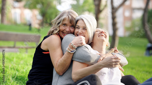 Фотография Three happy senior women friends laughing and embracing while sitting on green g