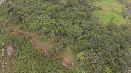 High-angle drone orbit over hikers at a mountain viewpoint, overlooking dramatic tropical valley and riverbed far below, lush interior landscape of Entre-Deux, Reunion Island.