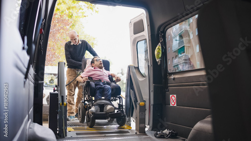 Man in wheelchair using a lift platform to enter an accessible vehicle, assisted by a caregiver, highlighting mobility and inclusion