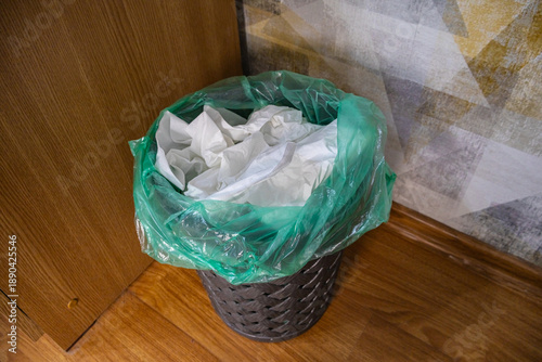 Indoor waste bin with green liner filled with crumpled paper