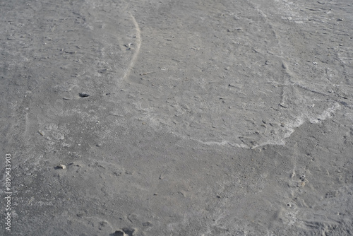 The gray backdrop of drying hand-mixed concrete. Waves of lime from river sand and the silhouettes of crushed stone edges appearing on the surface as the cement mortar dries. A beach vibe background. 