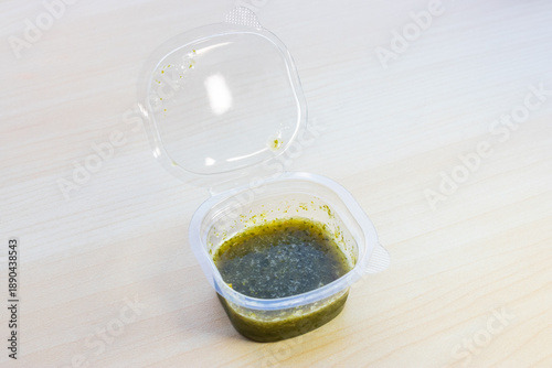 Spicy Thai seafood dipping sauce with chili, garlic, and lime in a small plastic container. Authentic zesty condiment for raw seafood, close-up view.