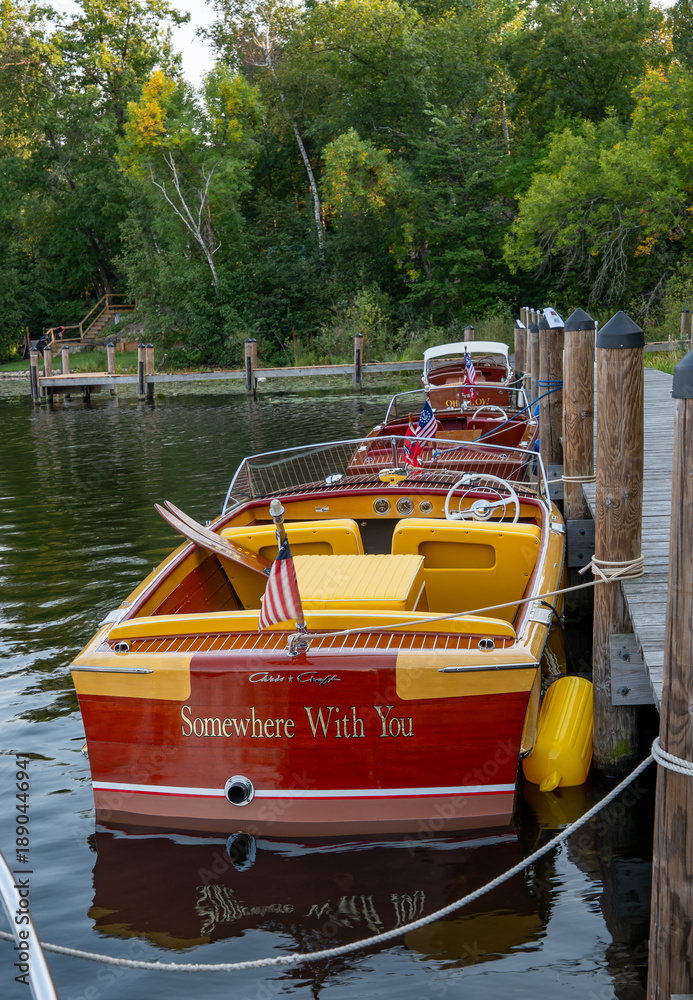 Fototapeta premium NISSWA, MN - 12 SEP 2024: Classic vintage wooden motorboat floating on the water, tied by rope to the dock on a Minnesota lake.