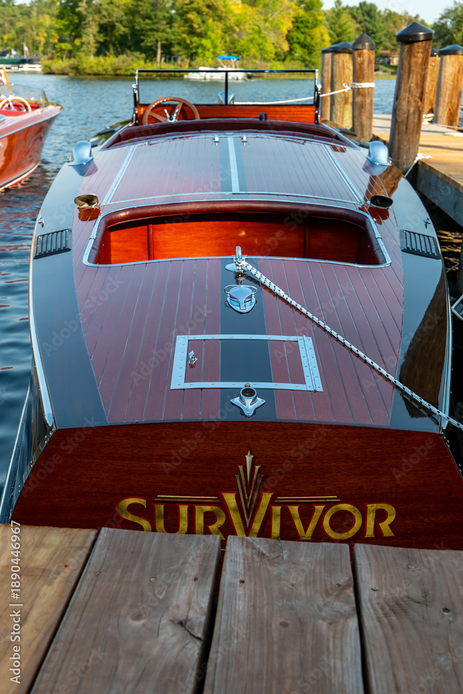 Fototapeta premium NISSWA, MN - 12 SEP 2024: Classic vintage wooden motorboat floating on the water, tied by rope to the dock on a Minnesota lake.