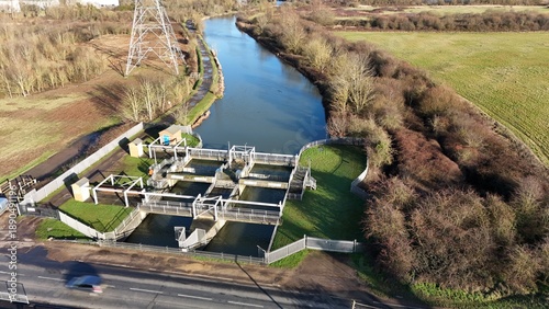 Aerial view of the reflective river glides past the sluice gate, bordered by winter's muted browns and greens, Hoddesdon, United Kingdom.