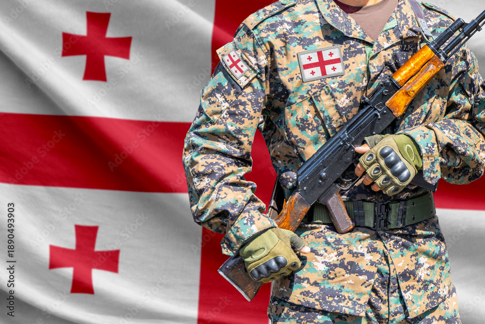 Fototapeta premium Georgia flag with soldier in military uniform holding assault rifle in front of it