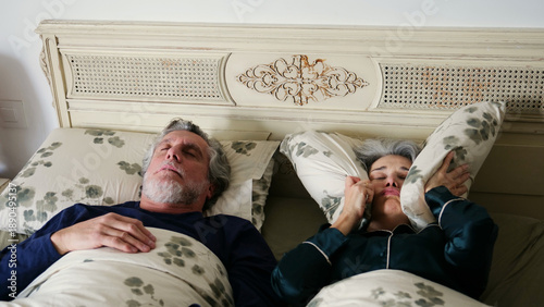 Bild auf Leinwand Older man snoring loudly while woman covers ears with pillow to block noise