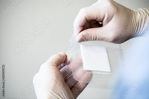 фотографія A healthcare worker peels the wrapping off of a hydrocolloid bandage against a w