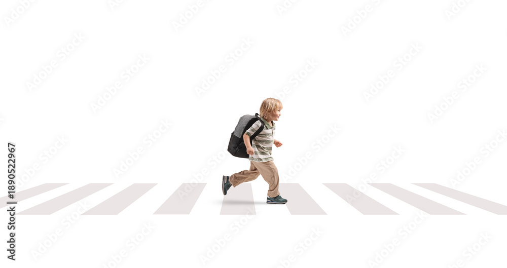 Fototapeta premium Full length profile shot of a young boy with a backpack running over a pedestrian crossing
