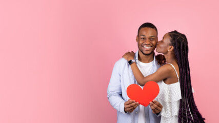 Couple in Love, Happy Emotions and St Valentine's day. Millennial black woman kissing smiling man, holding red heart and celebrate anniversary, isolated on pink background, banner, free copy space