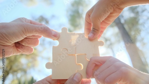 Obraz na plátne Hands assemble four wooden jigsaw pieces into a unified square on a bright backg