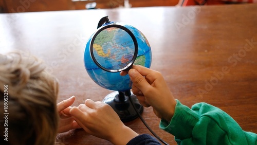 Bilde på lerret Child discovering the world, holding a magnifying glass and focusing on a globe,