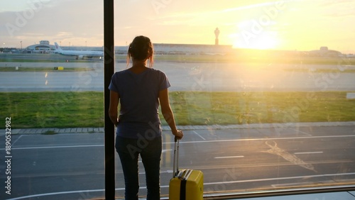 Tablou pe pânză Woman with luggage waiting for departure at airport gate, standing by large wind