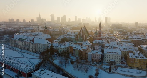 Cinematic drone view of Warsaw, Poland in winter. Establishing zoom in aerial shot of snowy Old Town landmarks. Royal Castle and Cathedral with the modern downtown business skyline in sunny haze