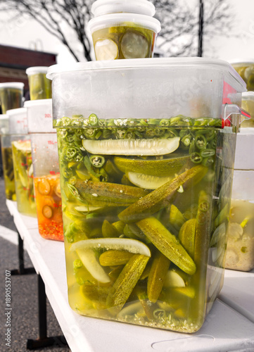 Pickled cucumbers and jalapeno peppers in a large plastic container at an outdoor market
