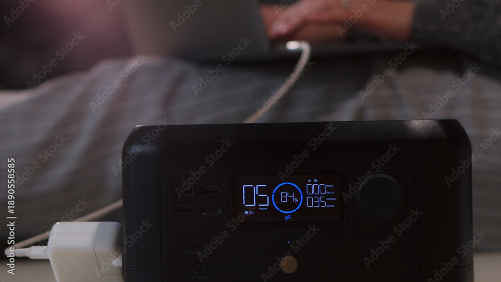 Fototapeta premium Portable power station charging a laptop while someone works remotely from a comfortable setting