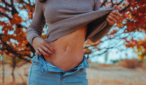 Woman lifting sweatshirt showing toned abs in autumn forest
