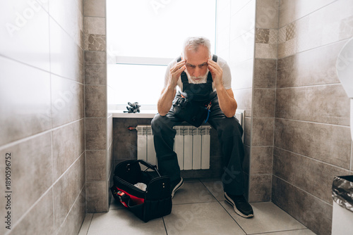 Fotografía Elderly gray haired man wearing workwear holding and using tools repairing sipho