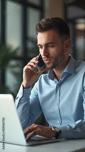 Male business trainer talking on phone while working with laptop in office.