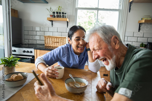 Caregiver and senior man laughing over breakfast at home