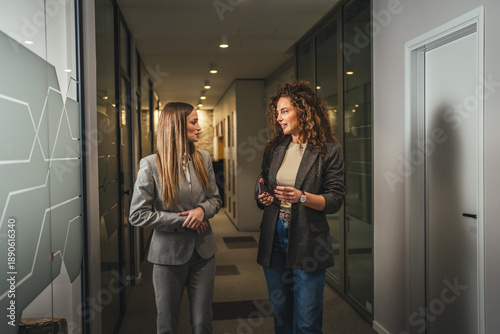 Tablou pe pânză Businesswomen walking and conversing in modern office corridor