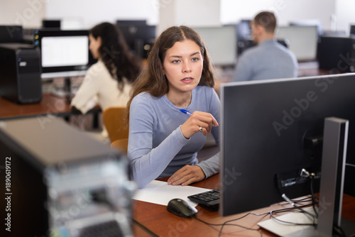 Foto In group of students attending computer courses, female student looks at monitor screen and does performs educational control work, write down note in notebook, write down most important points