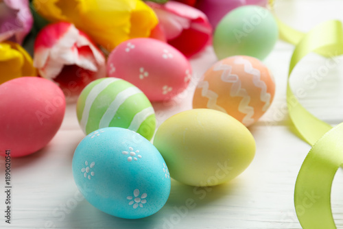 Painted Easter eggs, beautiful tulips and ribbon on white wooden table, closeup