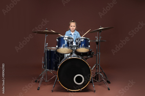 Obraz na plátně Little girl learning how to play drums on brown background