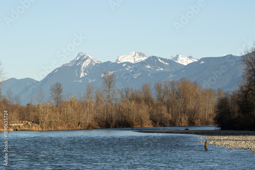 Angler fishing in the Chilliwack river in a sunny winter day with the mountains in the background.