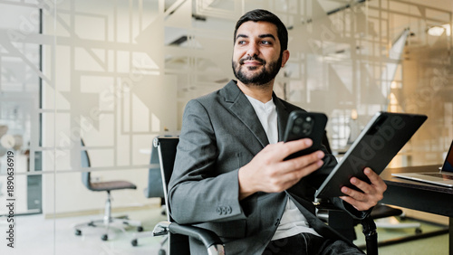 Photos Young man sits in modern office and uses smartphone while looking ahead with a f