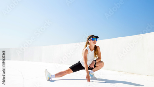 Canvas Print Woman stretches on a sunny day in an outdoor area near a bright blue sky and a w