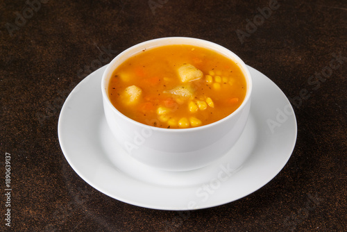 A bowl of corn soup with potato on a saucer on a dark table